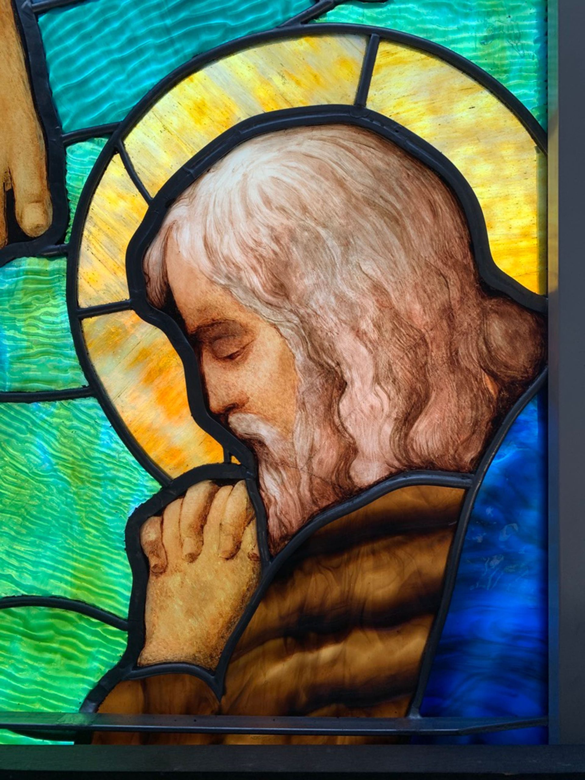 A close-up of stained glass of a saint praying.