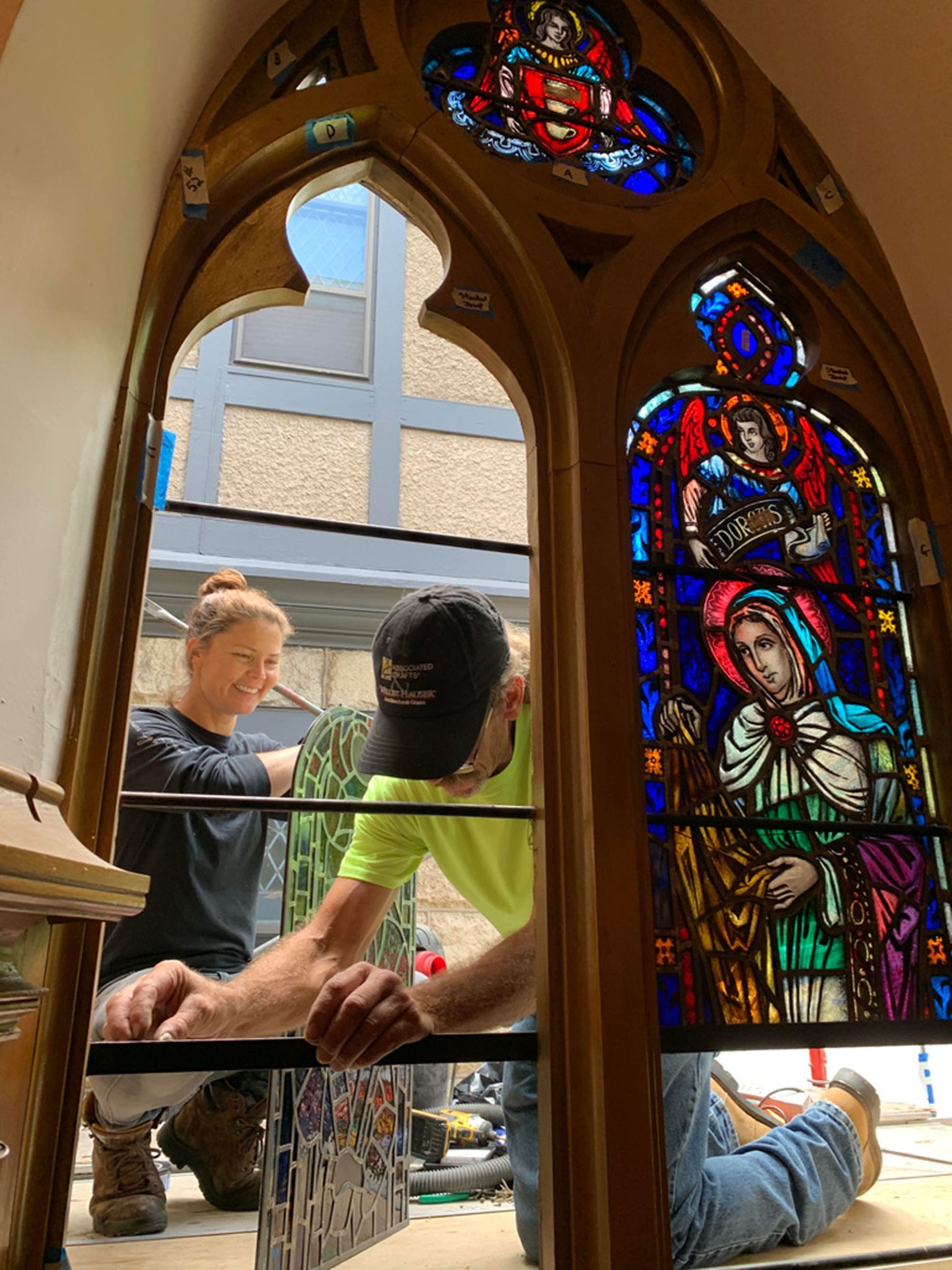 Two craftsman install stained glass in a church.