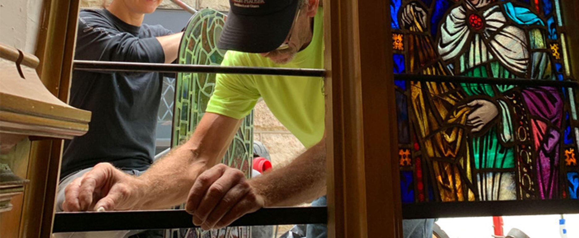 Two craftsman install stained glass in a church.