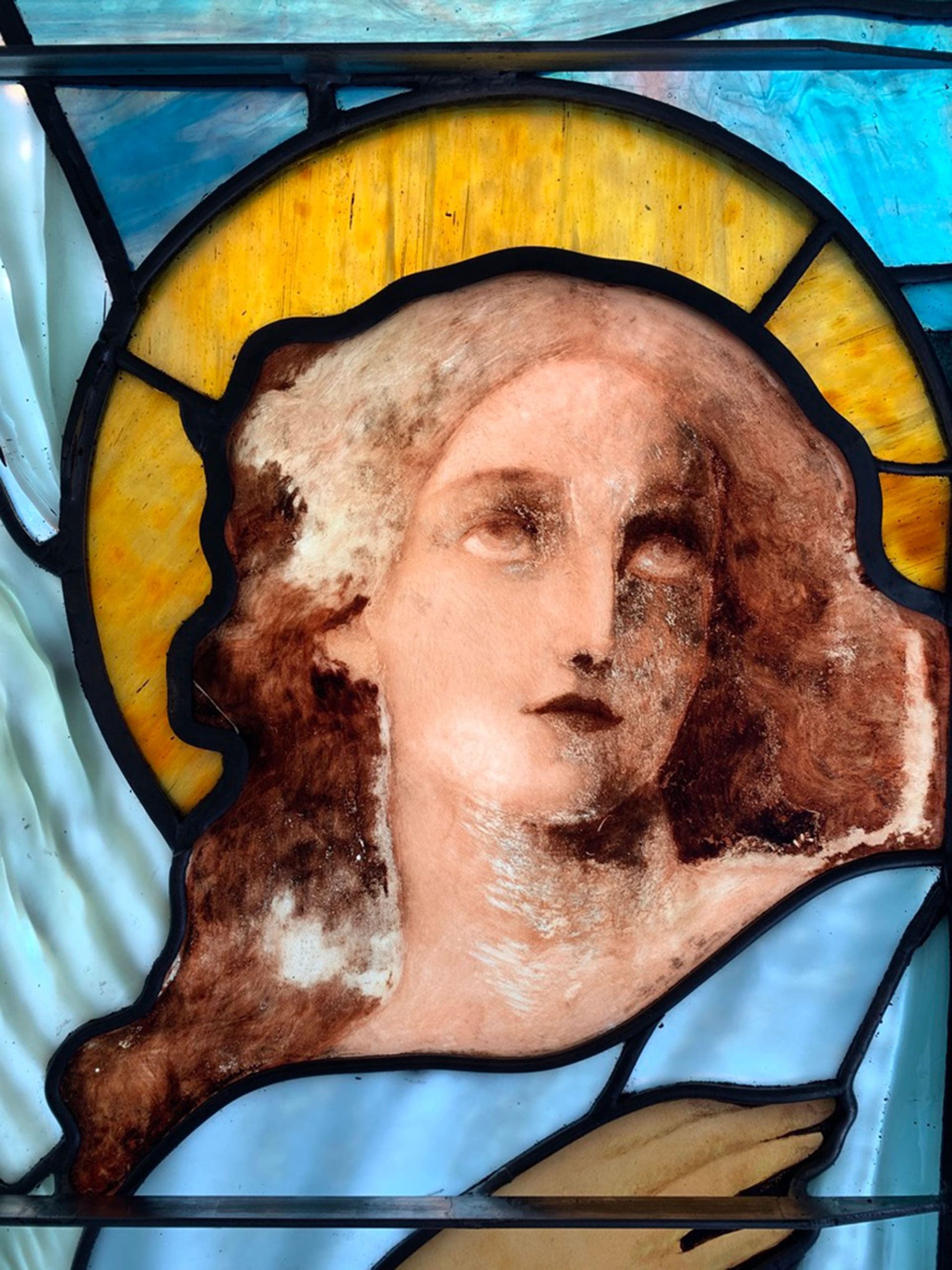 Stained glass of a female saint. The stained glass is damaged and in need of repair.