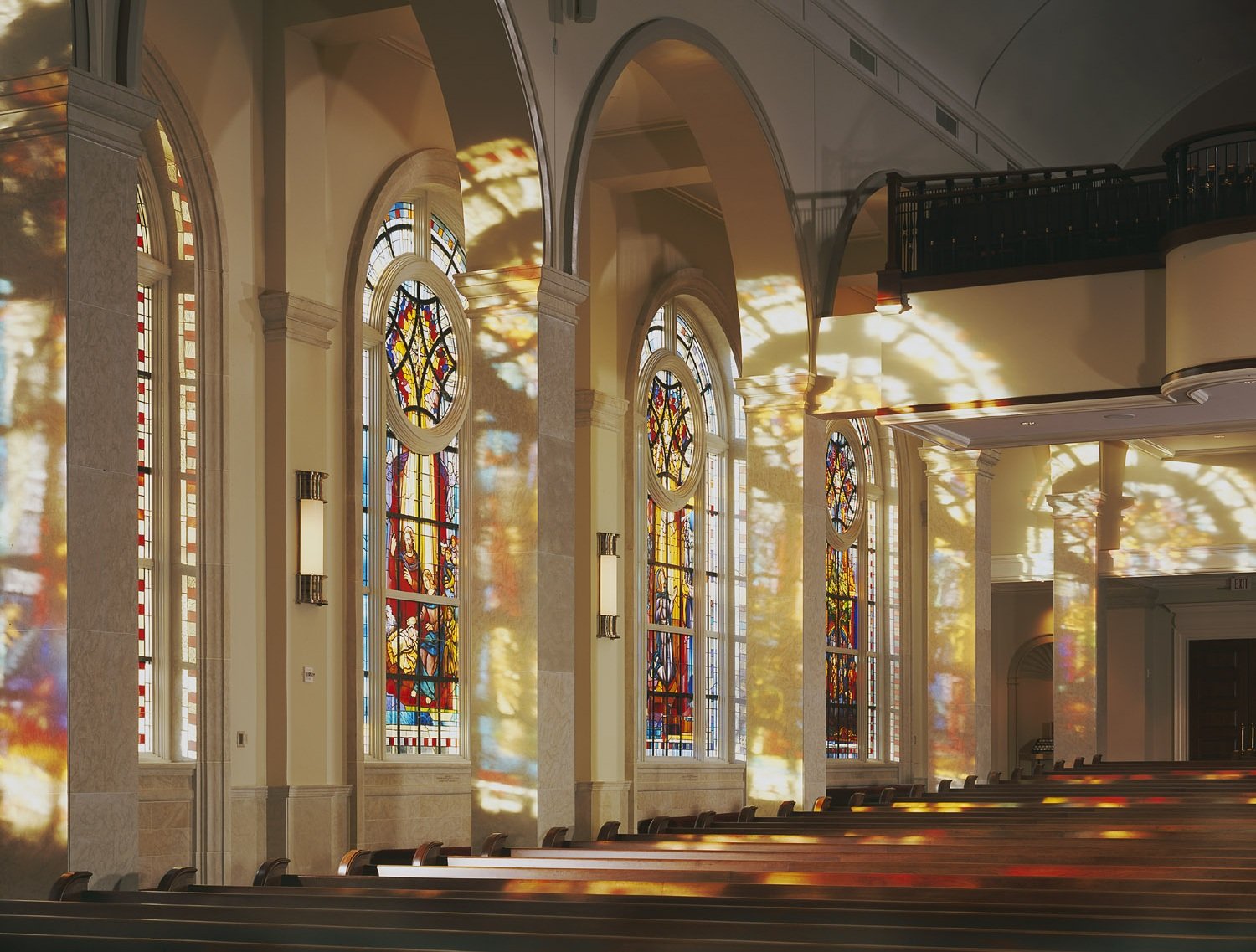 Stained glass windows casting colorful reflections in a church interior, showcasing Willet Studios' craftsmanship in art glass design for sacred spaces.