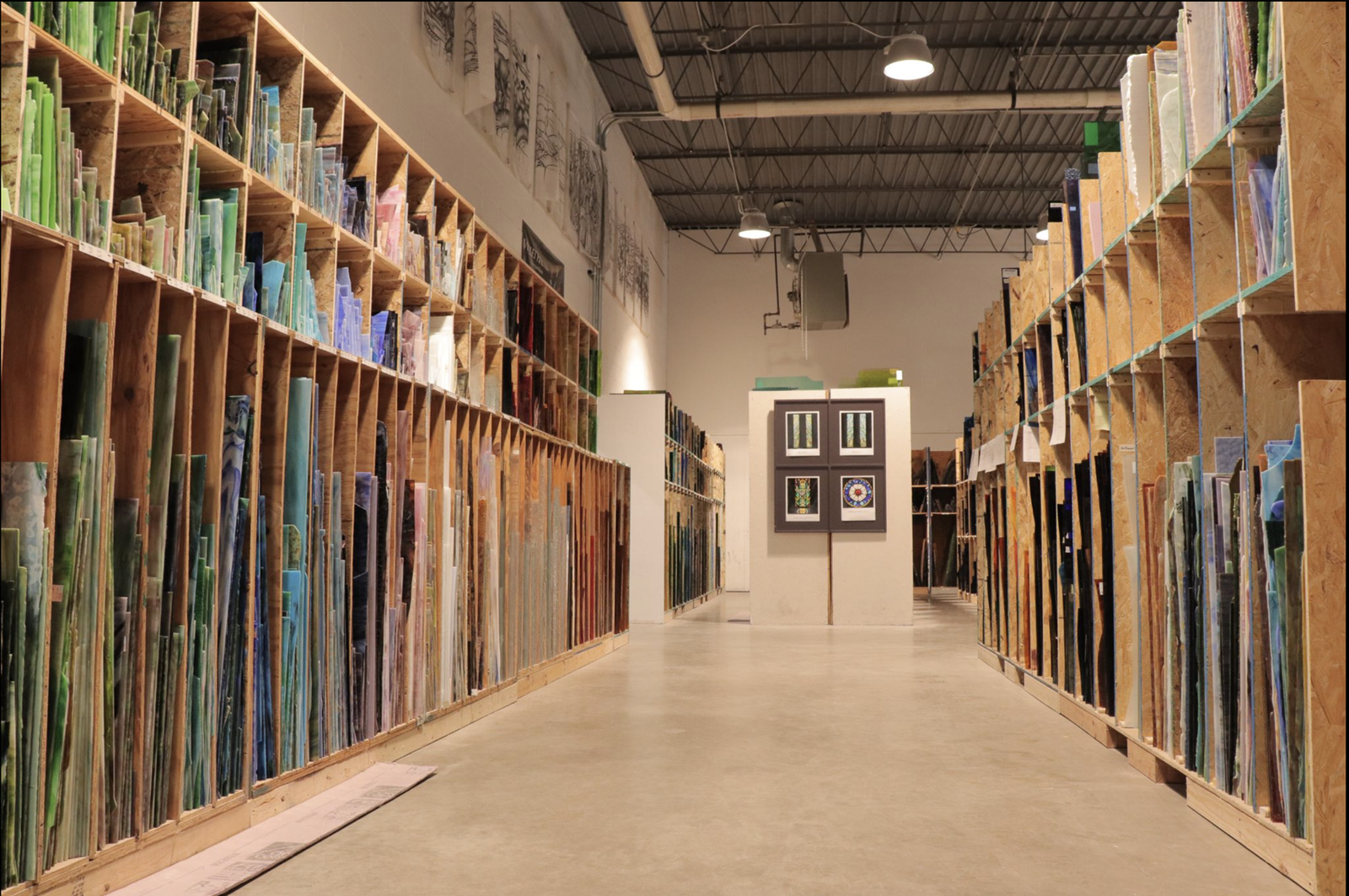 Glass inventory display in a studio showcasing various colors and textures of glass panels, with framed artwork in the center, emphasizing custom glasswork and craftsmanship for high-end interiors.