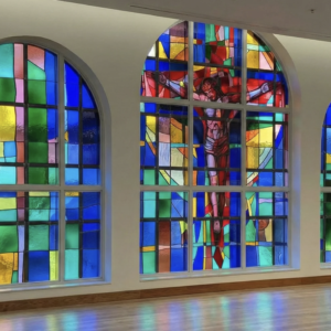 High-end stained glass window design featuring vibrant colors and abstract patterns, showcasing a central figure of Christ on the cross, installed in a modern architectural space.