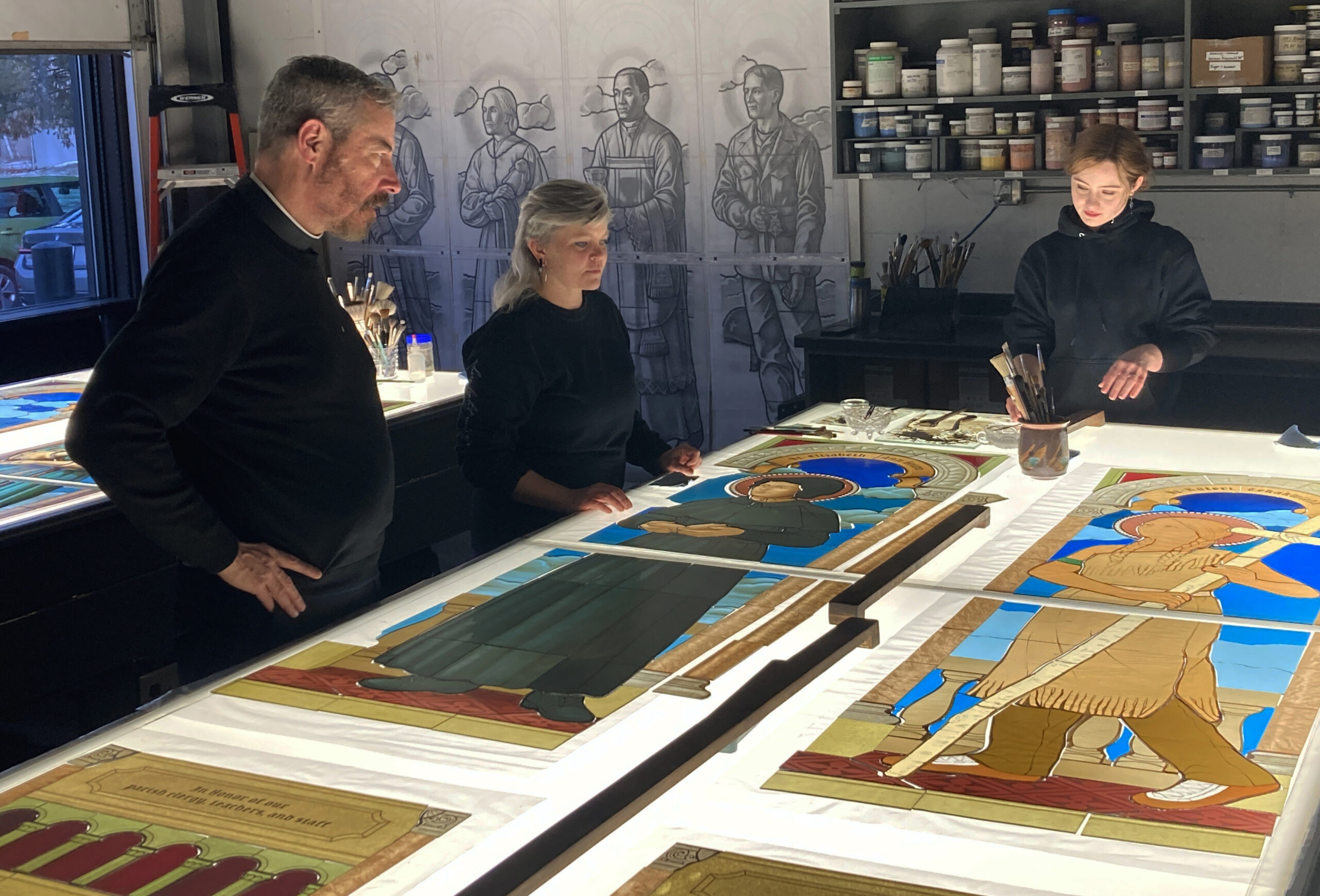 Collaborative stained glass artists reviewing colorful panels in Willet Studios workshop, showcasing craftsmanship and design integration.