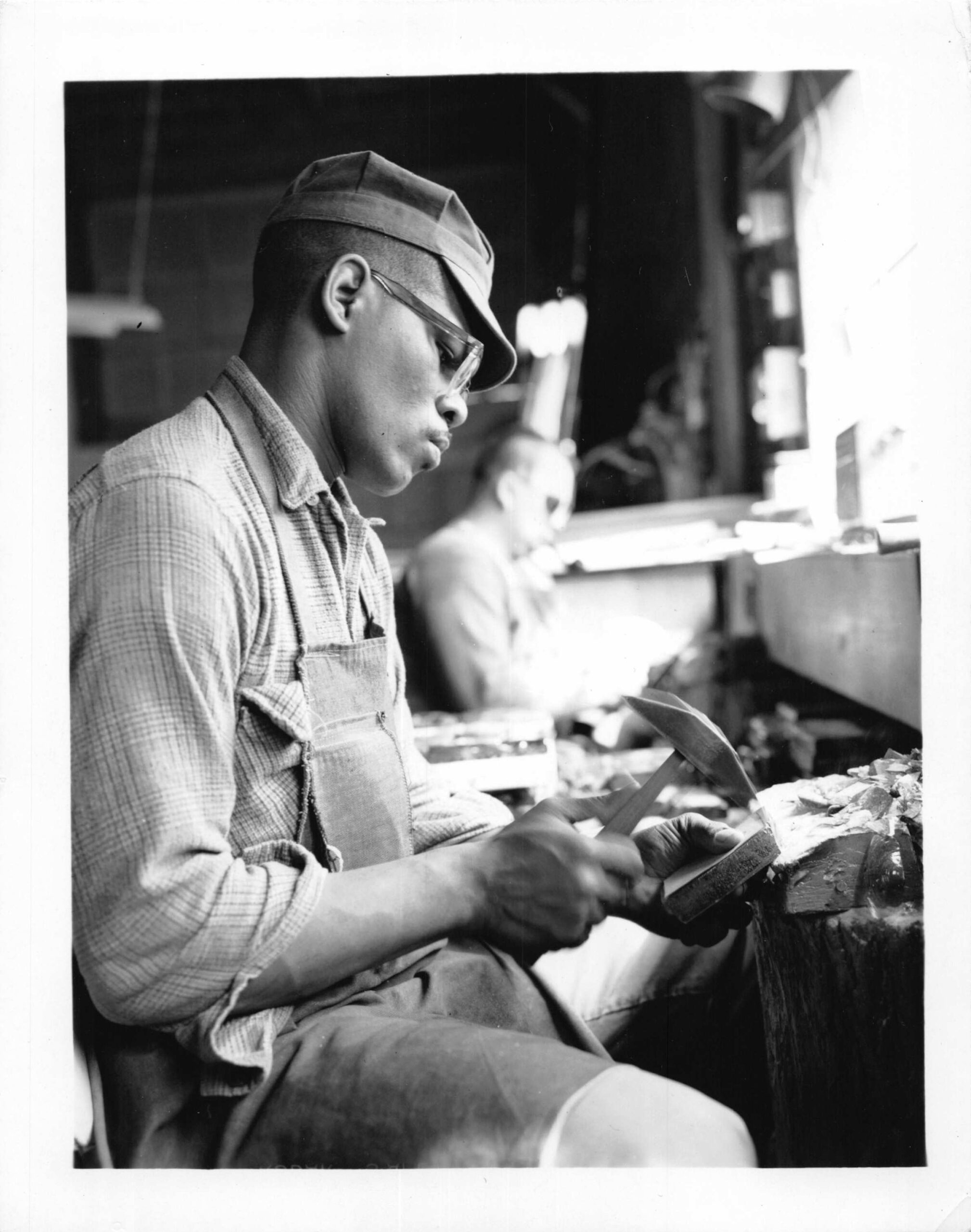 Craftsman shaping stained glass with tools in a workshop, emphasizing artistry and craftsmanship at Willet Stained Glass Studios.