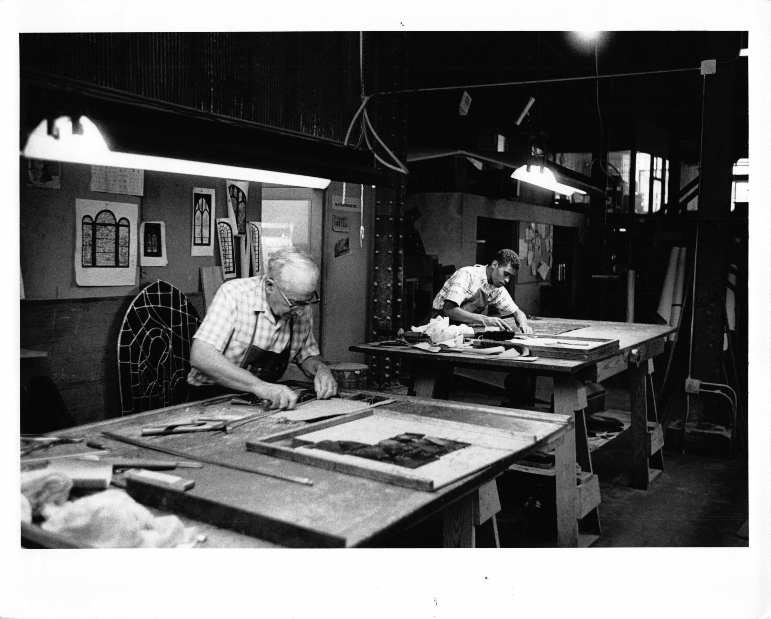 Artisans working on stained glass projects in a workshop, showcasing craftsmanship and design excellence in stained glass artistry.