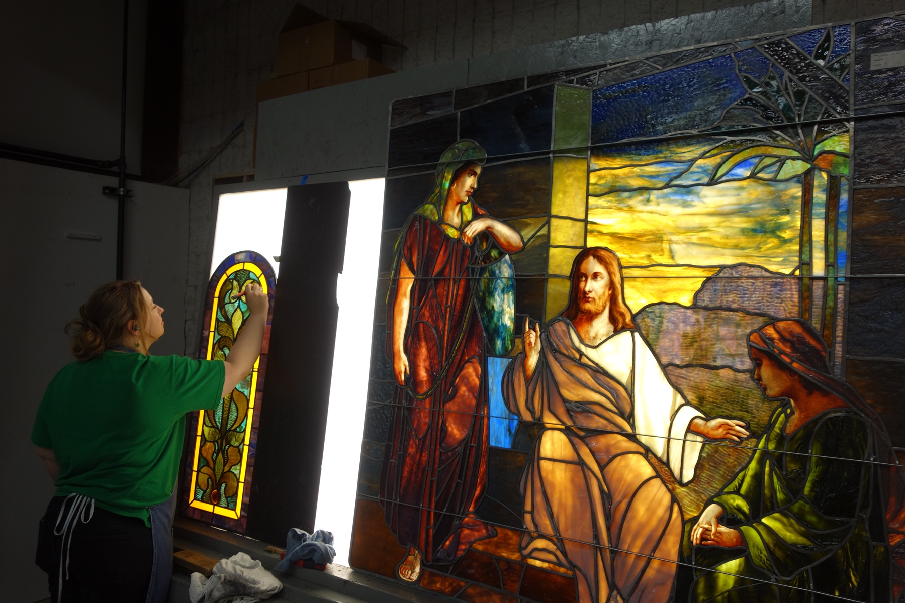 Woman painting a stained glass window in a studio, showcasing traditional craftsmanship and artistry at Willet Studios.