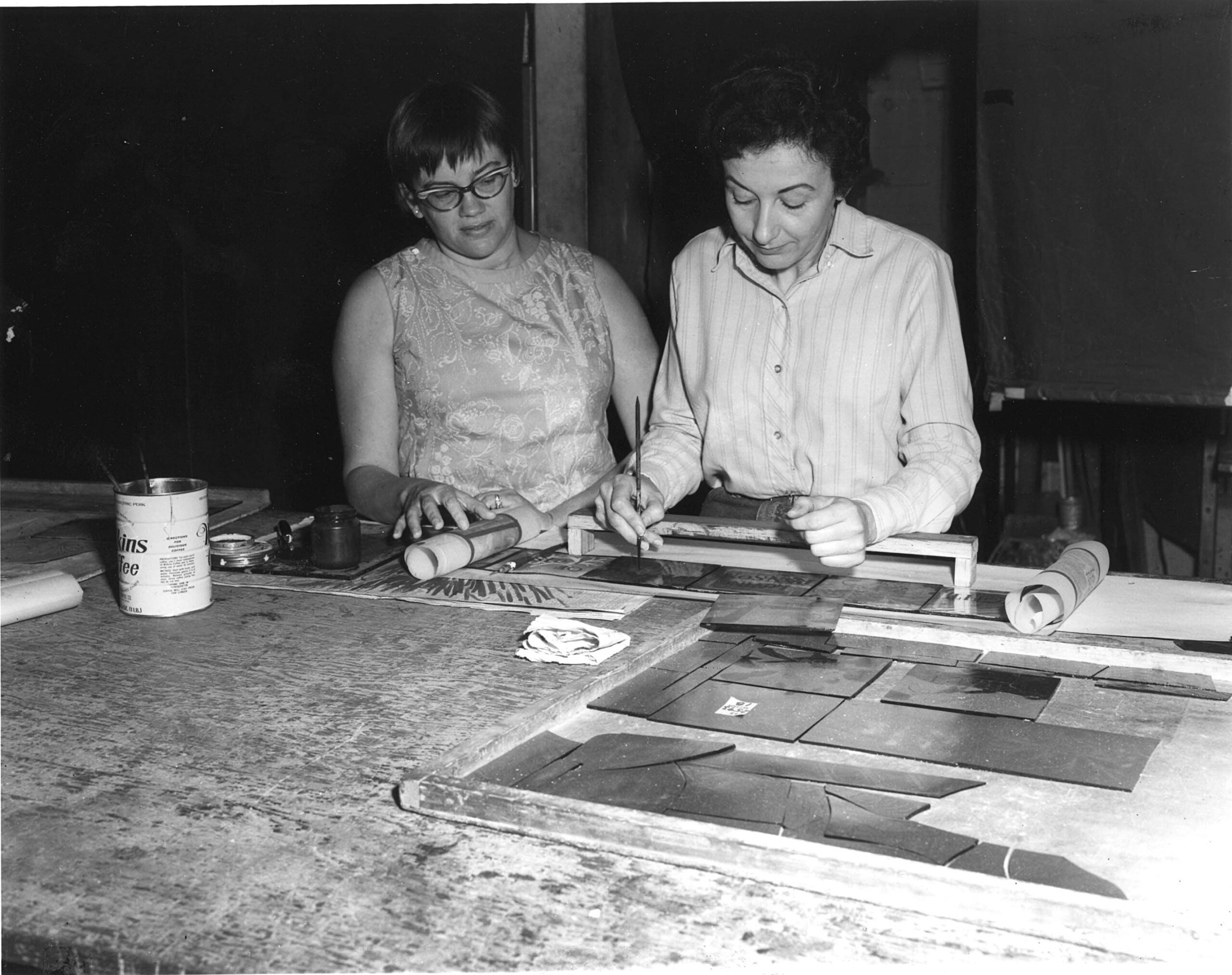 Women working on stained glass design, surrounded by tools and materials, showcasing craftsmanship at Willet Stained Glass Studios.
