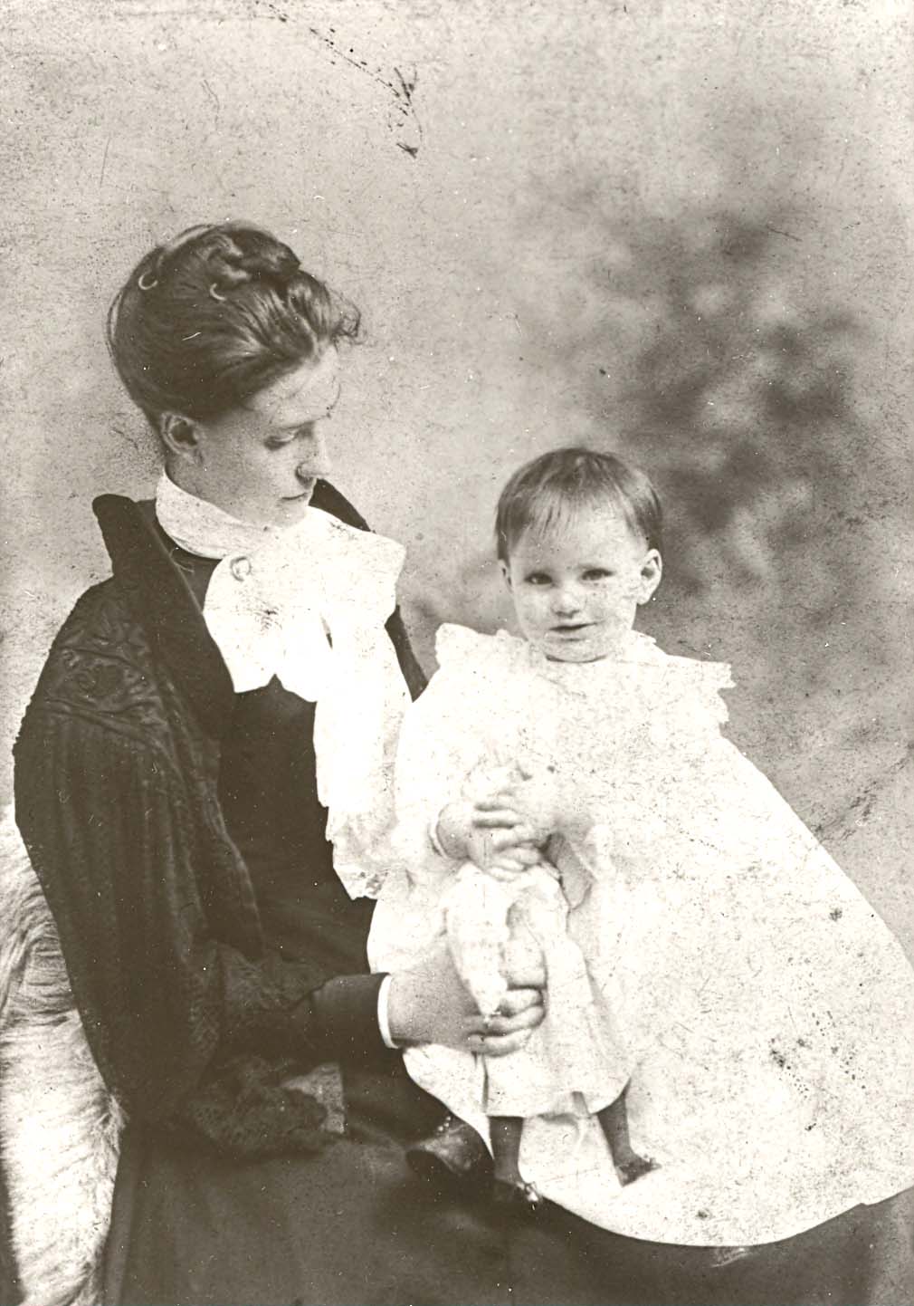 Woman in historical attire holding a child in a white dress, symbolizing family legacy and tradition in the context of Willet Stained Glass Studios' history and craftsmanship.