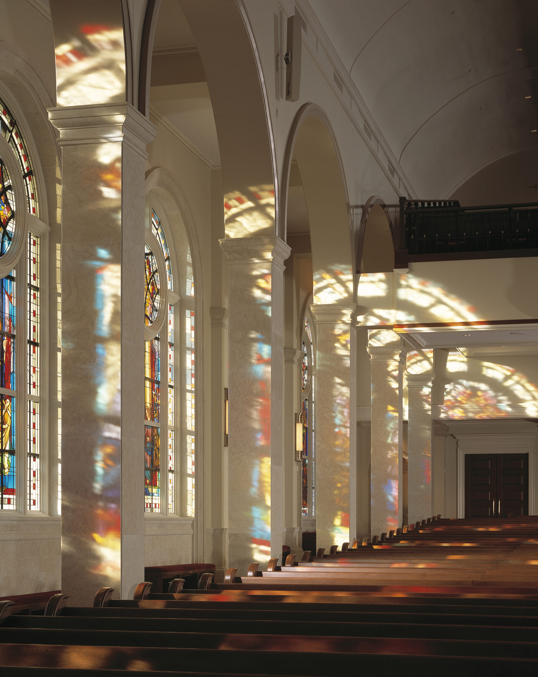 Interior of Peachtree Road United Methodist Church showcasing vibrant stained glass windows and colorful reflections on the walls, emphasizing architectural beauty and serene atmosphere.