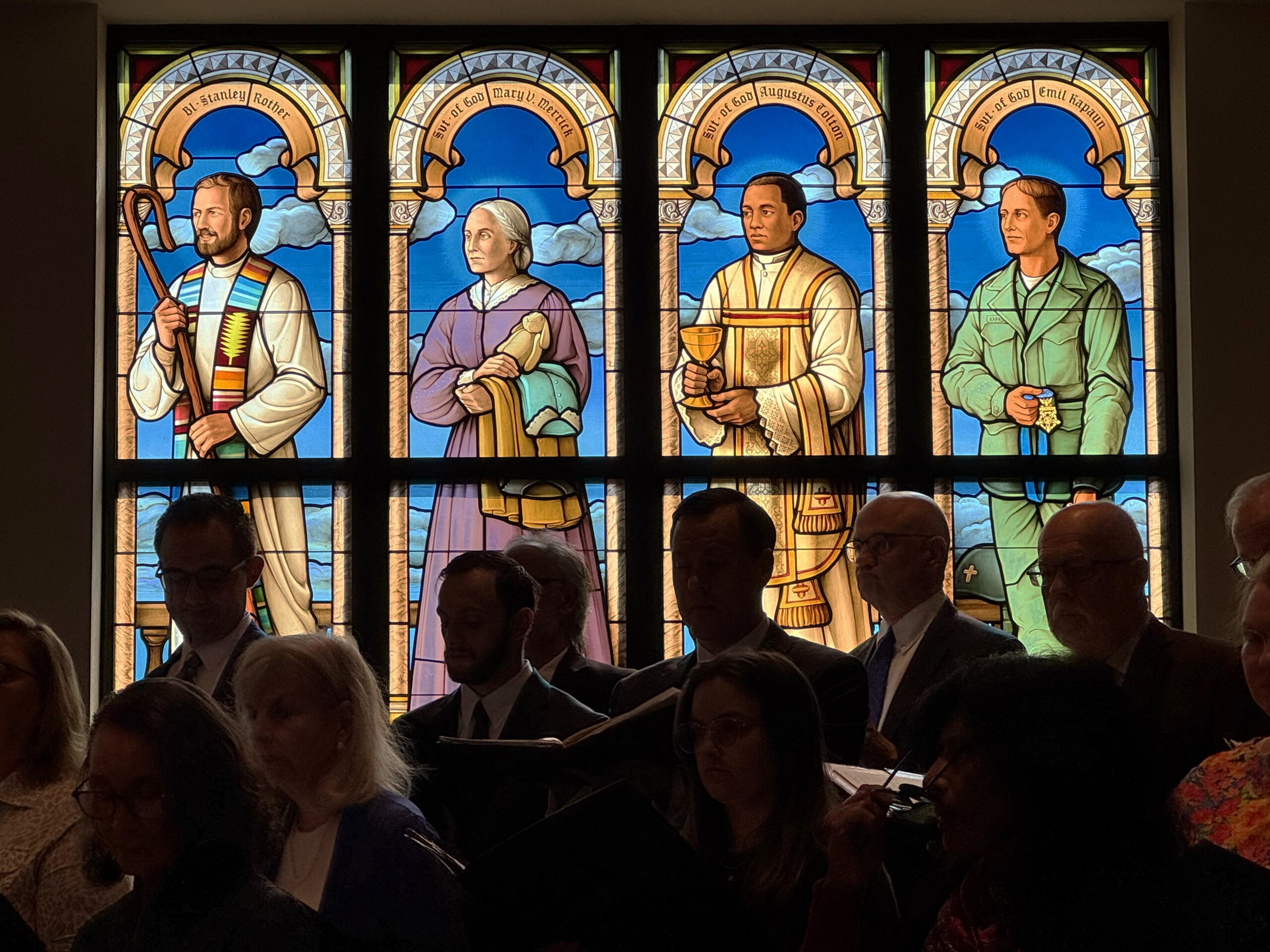 Stained glass window featuring four figures representing faith and service, highlighting clergy and a soldier, in a worship setting at Willet Stained Glass Studios.
