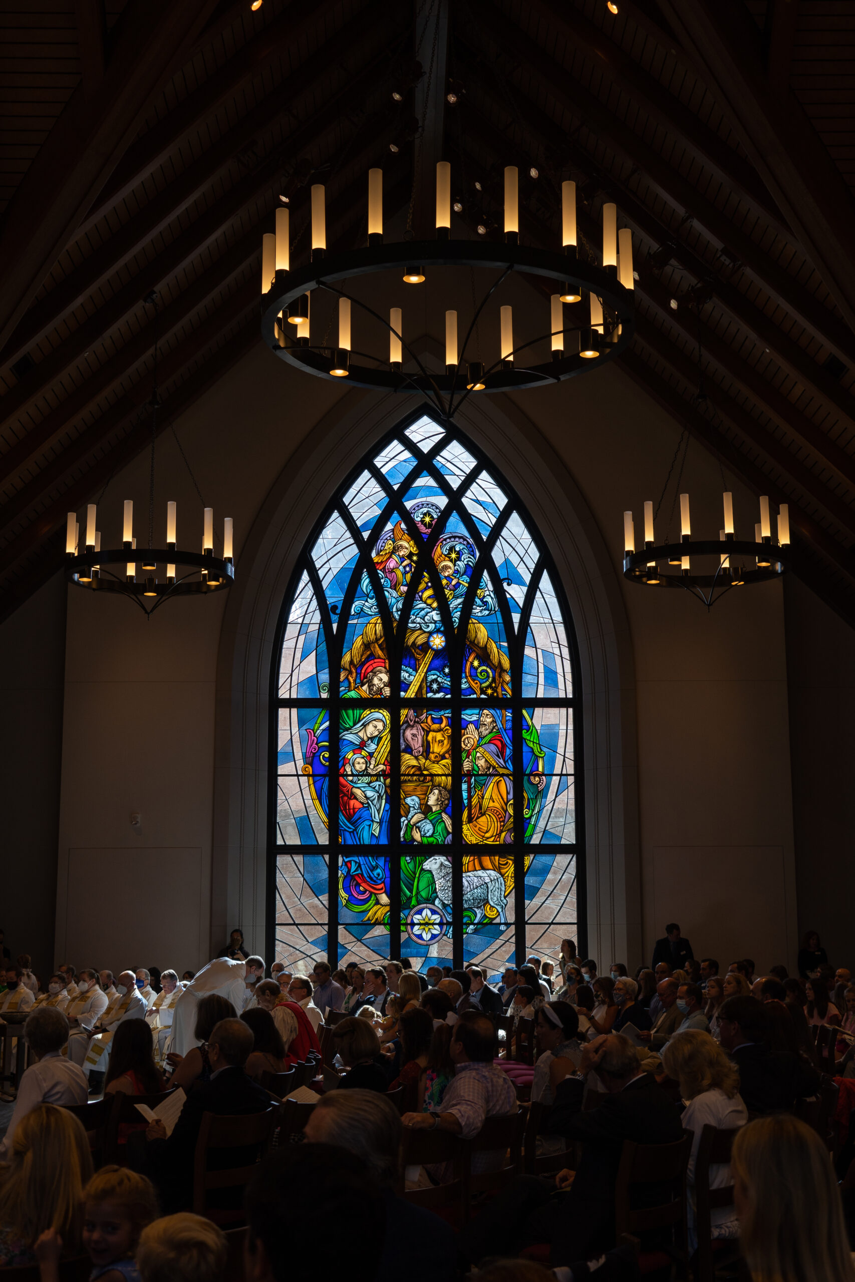 Stained glass window depicting a vibrant scene of religious figures, illuminating a congregation during a worship service in a church setting, showcasing the artistry of Willet Stained Glass Studios.