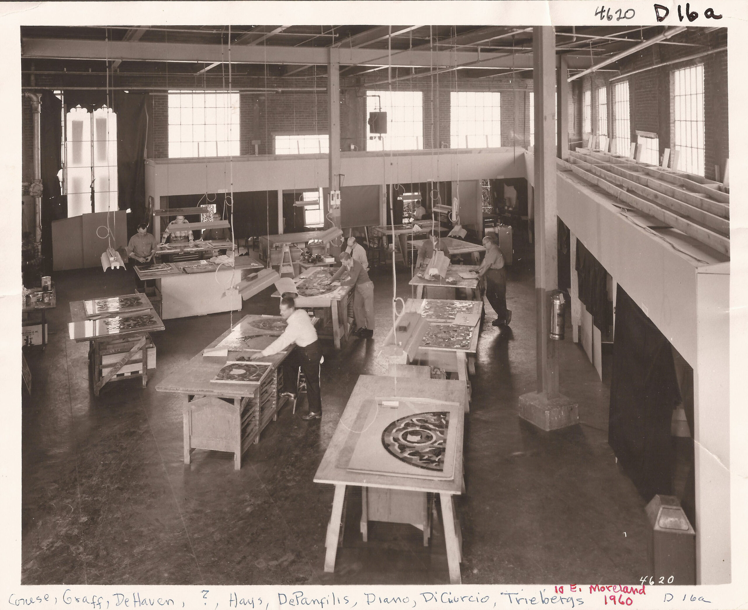 Historic stained glass studio workspace with artisans collaborating on stained glass projects, showcasing craftsmanship and design excellence central to Willet Stained Glass Studios' legacy.