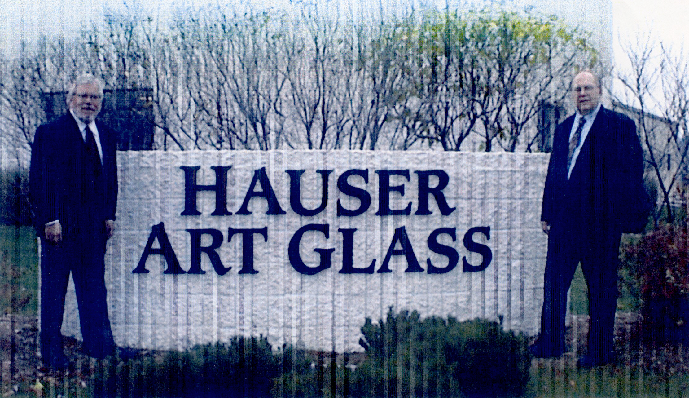 Two men in suits standing beside a sign reading "HAUSER ART GLASS," representing the legacy of stained glass artistry and craftsmanship associated with Willet Stained Glass Studios.