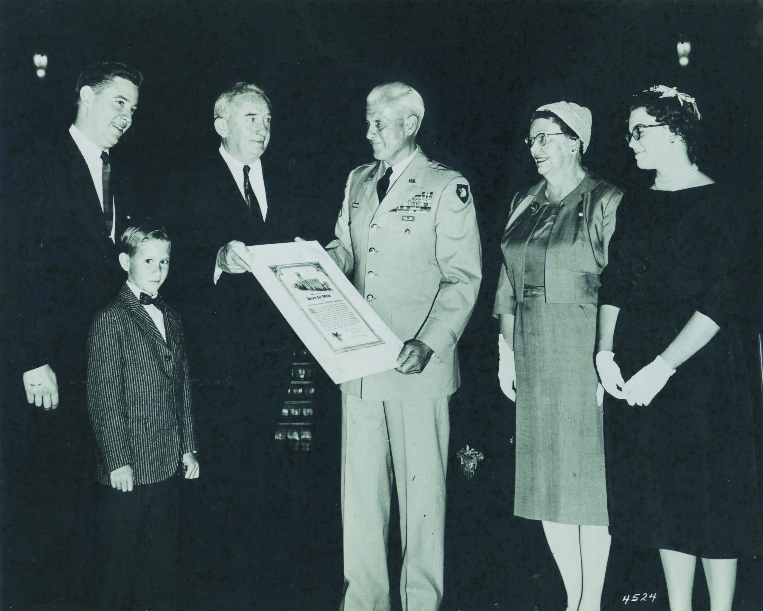 Henry Lee Willet receiving an award, surrounded by five individuals including a boy in a suit, a military officer in uniform, and three women in formal attire, highlighting the legacy of Willet Stained Glass Studios.