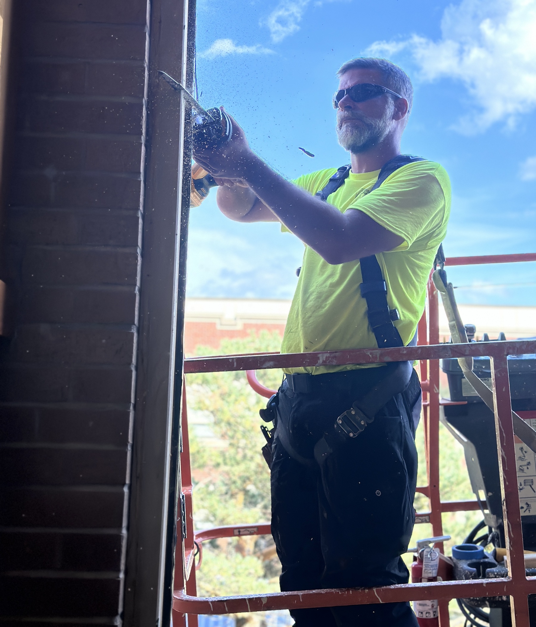 Worker in safety gear using power tools on scaffolding for stained glass installation, emphasizing hands-on work and professionalism at Willet Studios.