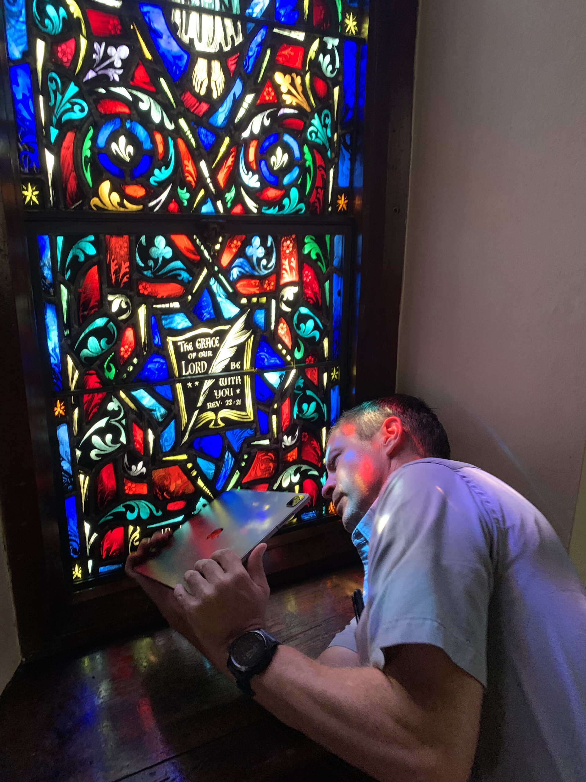 Man examining stained glass window with detailed patterns and vibrant colors, documenting installation for stained glass craftsmanship.