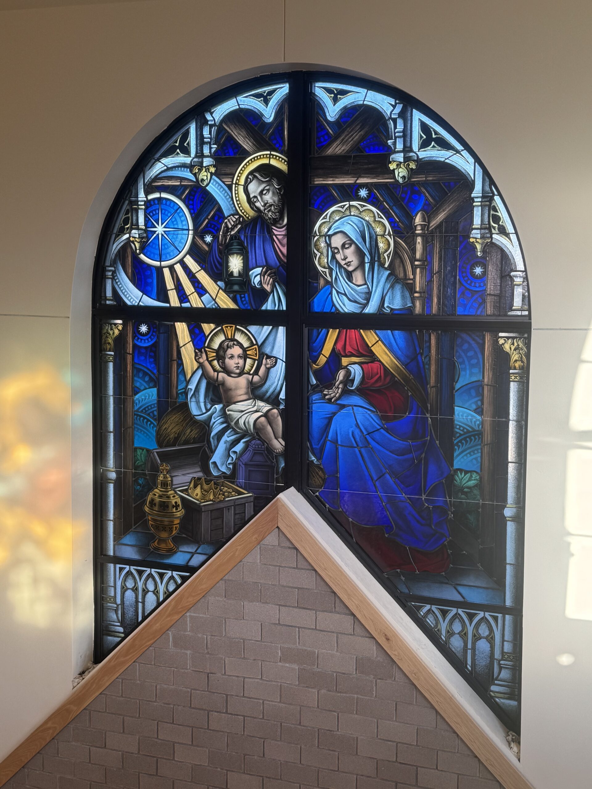 Stained glass window depicting the Holy Family: Mary and Joseph with the infant Jesus, illuminated by vibrant blue and gold hues, symbolizing faith and inspiration in a religious space.