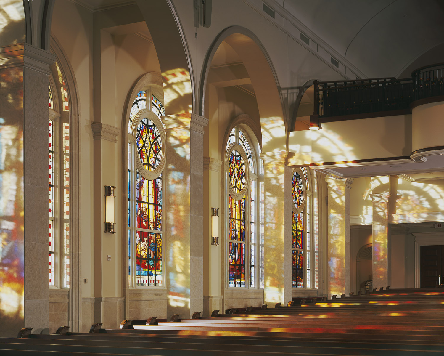 Stained glass windows casting colorful reflections in a church interior, enhancing the sacred space and illustrating Willet Stained Glass Studios' artistry.