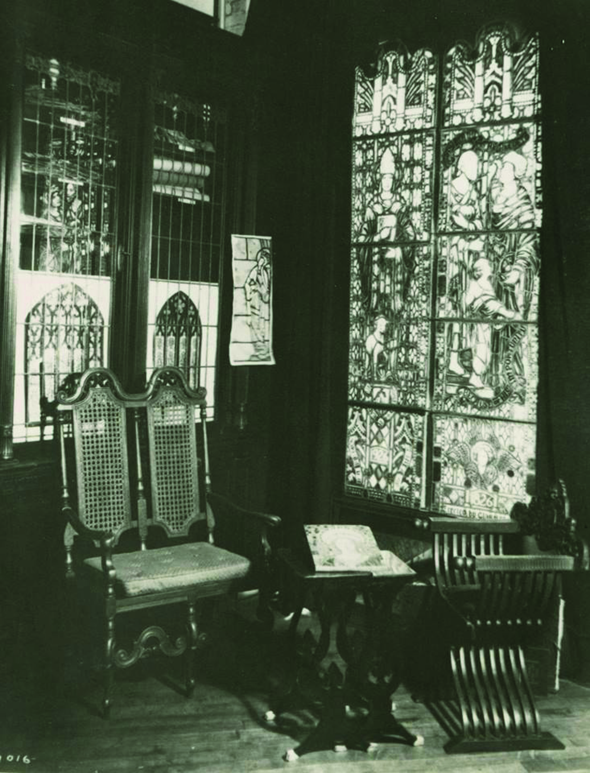 Historic interior of Willet Stained Glass Studios featuring intricate stained glass windows, antique wooden chairs, and a small table, emphasizing the studio's artistry and craftsmanship in stained glass design.