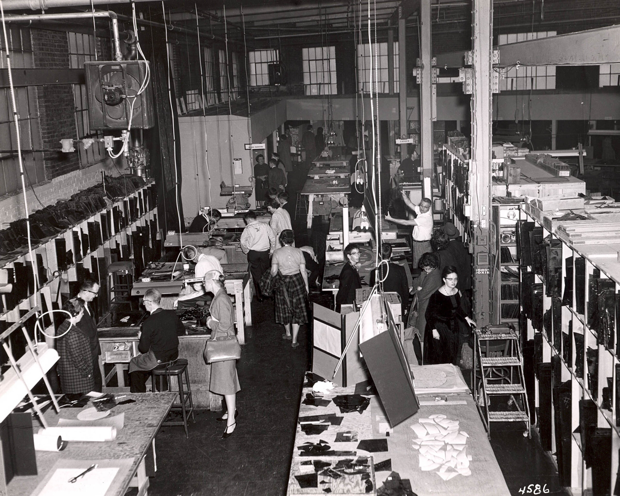 Historic Willet Stained Glass Studios workshop, showcasing artisans engaged in stained glass production, with workstations filled with glass pieces and tools, reflecting the studio's craftsmanship and legacy.