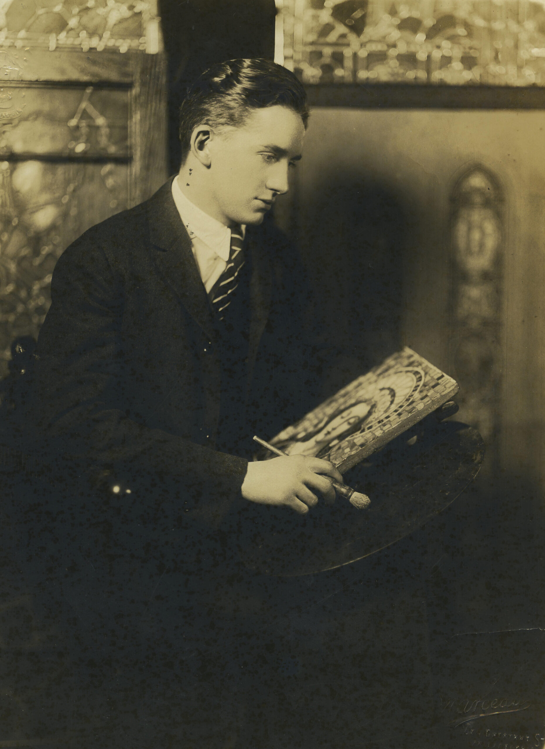 Young artist sketching stained glass design, seated with brush and palette, historical context related to Willet Stained Glass Studios' legacy and craftsmanship.