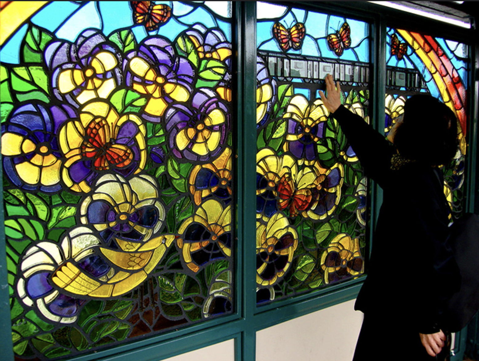 Stained glass window featuring vibrant flowers and butterflies, with a person interacting with the artwork, showcasing custom glasswork and artistic craftsmanship.