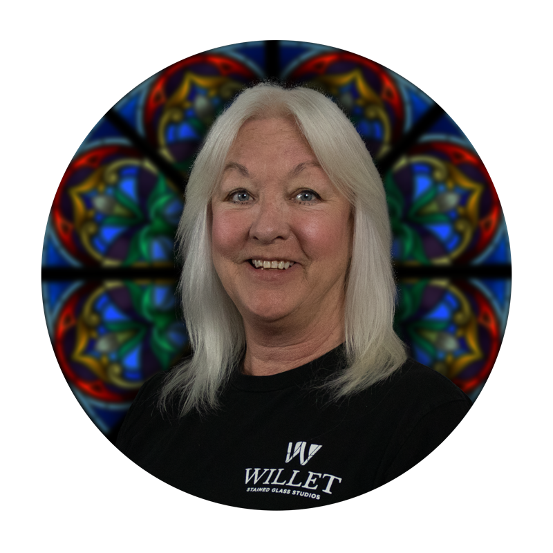 Brenda Dickinson, Glazing Specialist at Willet Stained Glass Studios, smiling with a stained glass background.