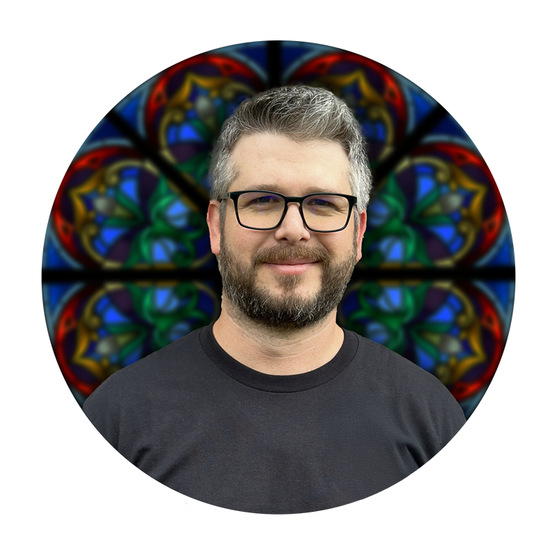 Daniel White, Studio Manager at Willet Stained Glass Studios, smiling in front of a colorful stained glass background.