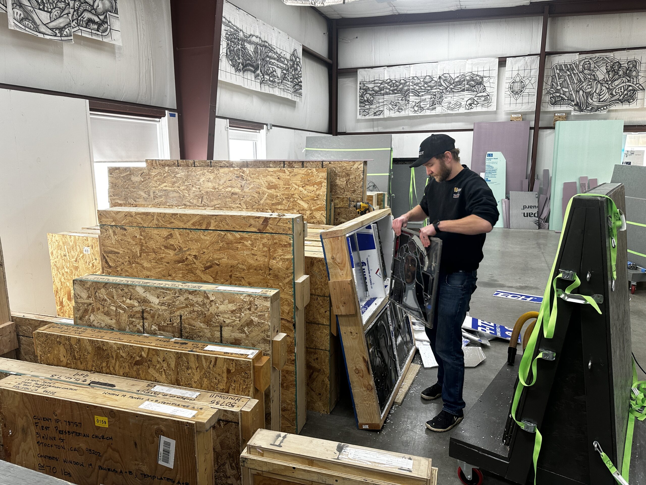 Man carefully handling a stained glass panel while organizing custom-built crates in a climate-controlled storage facility for historic stained glass preservation.