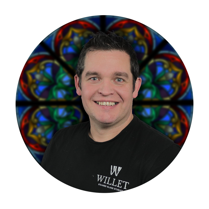 Jared Heyer, Glazing Lead at Willet Stained Glass Studios, smiling against a backdrop of colorful stained glass design.