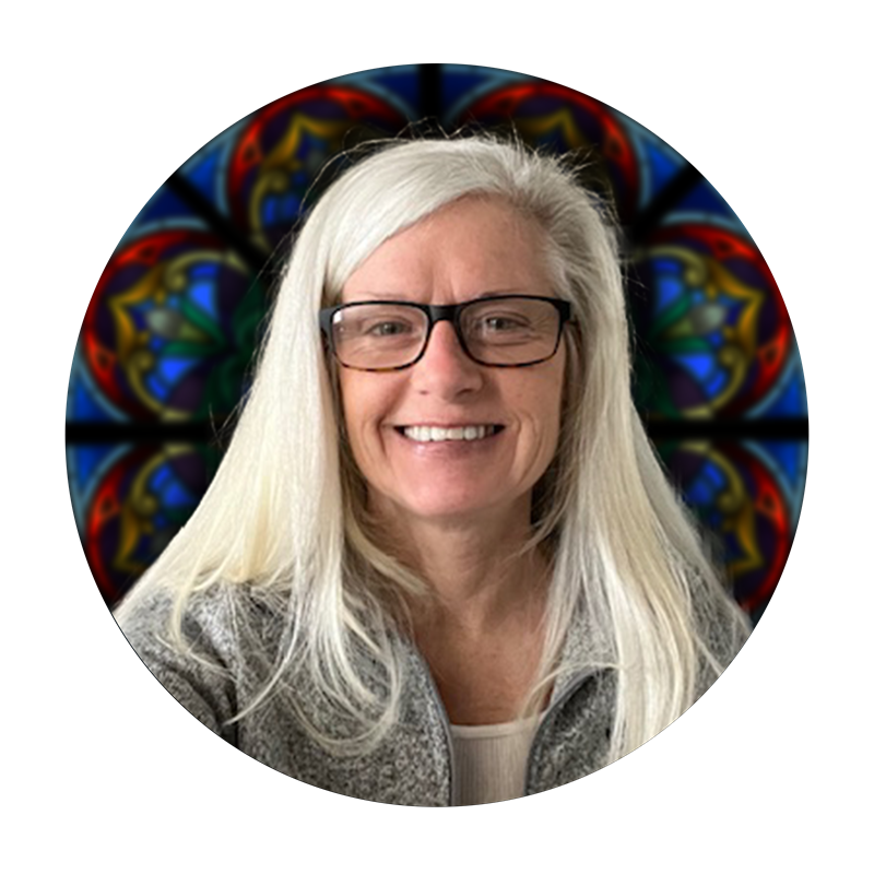 Kathy Murphy, Production Lead at Willet Stained Glass Studios, smiling in front of a colorful stained glass backdrop.