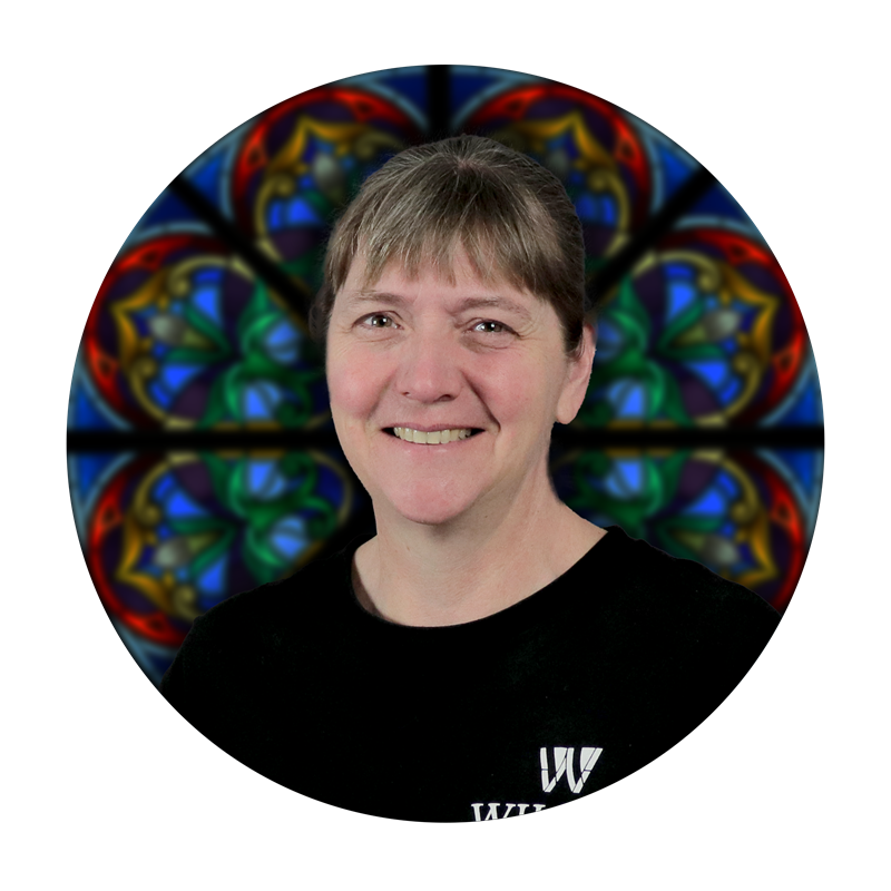 Lori Wendt, Glass Cutting Specialist at Willet Stained Glass Studios, smiling in front of a colorful stained glass background.