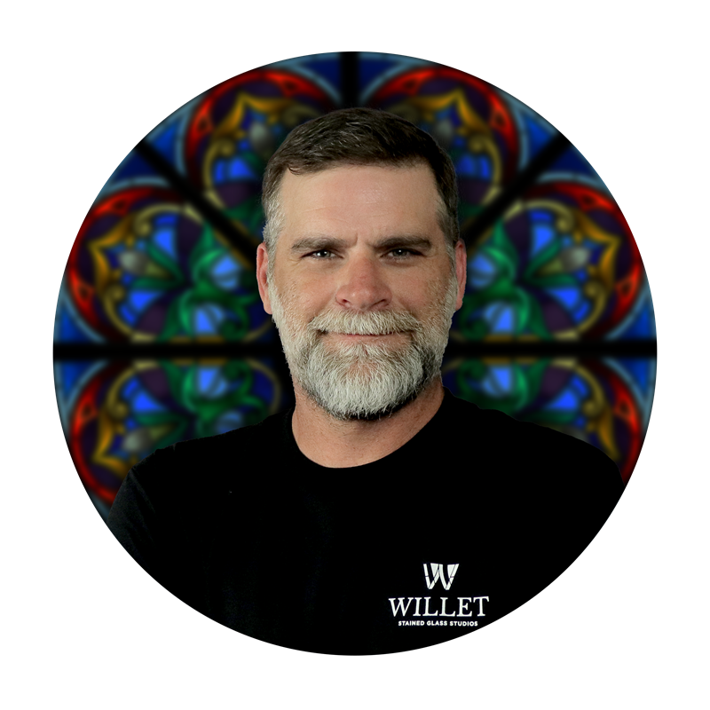 Mark Huerkamp, Project Manager at Willet Stained Glass Studios, smiling against a colorful stained glass background.