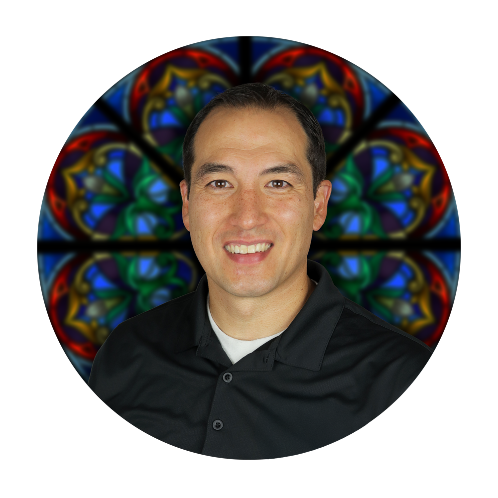 Michael Mills, President of Willet Stained Glass Studios, smiling in front of a stained glass window backdrop, showcasing the studio's artistry and craftsmanship.