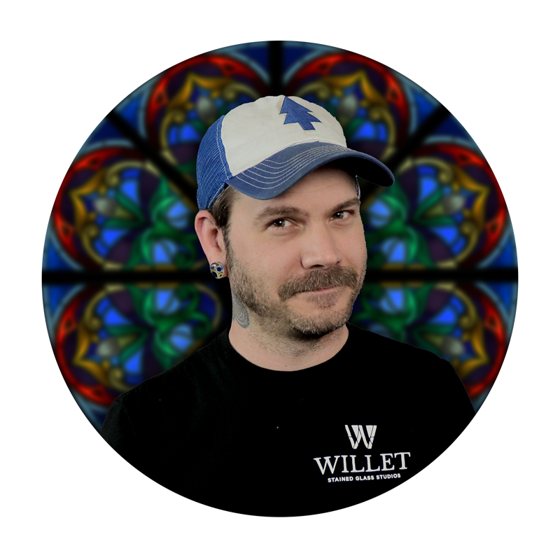 Oisín Mac Suibhne, Fusing Specialist at Willet Stained Glass Studios, with stained glass background.