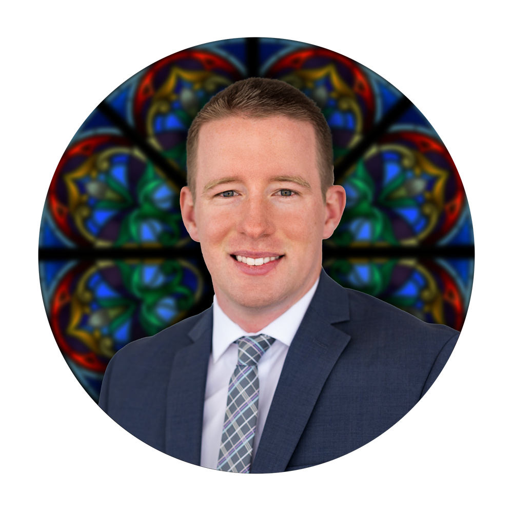Tanner Hughes, Director of Human Resources at Willet Stained Glass Studios, with a stained glass window backdrop, symbolizing craftsmanship and artistry in stained glass design.