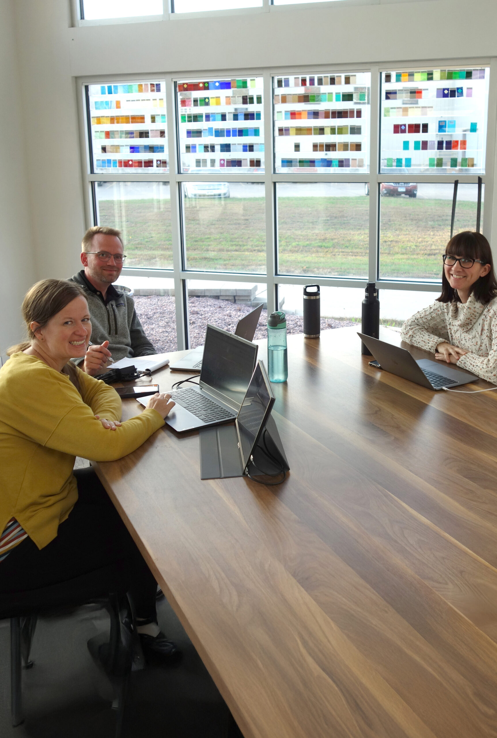 Team meeting at Willet Stained Glass Studios, showcasing collaboration and creativity, with stained glass samples visible in the background.