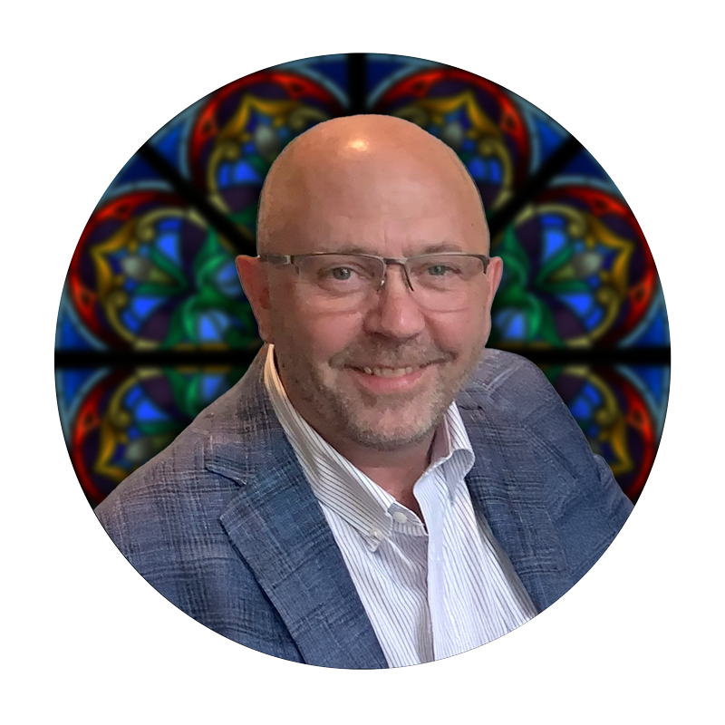 Brad Fries, Studio Consultant at Willet Stained Glass Studios, smiling in front of a colorful stained glass background, showcasing artistry and craftsmanship.