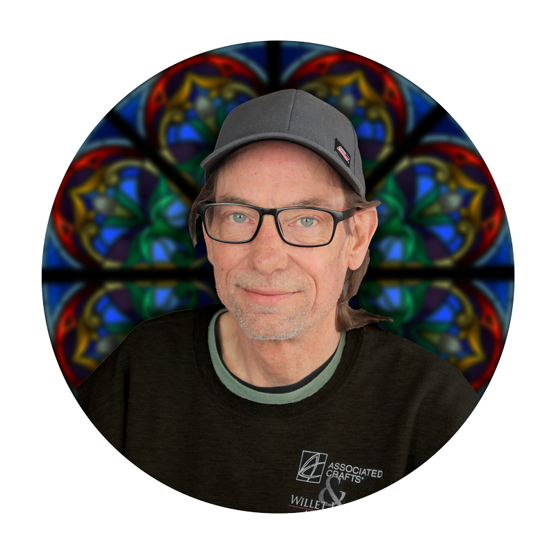Greg Wignes, Master Craftsman at Willet Stained Glass Studios, with stained glass background.