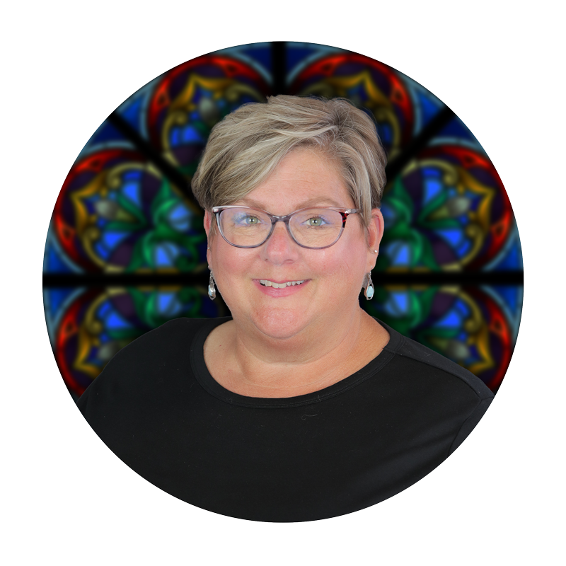 Julie Biggerstaff, Historical Archivist at Willet Stained Glass Studios, with stained glass background.