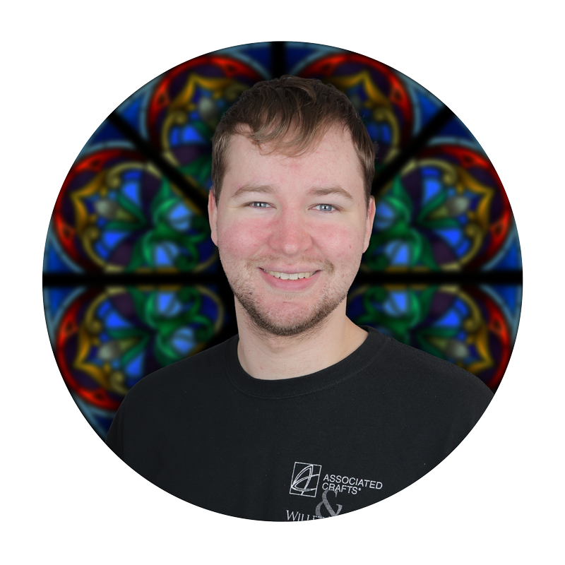 Kieran McDonnell, post-production specialist at Willet Stained Glass Studios, smiling in front of a colorful stained glass background.