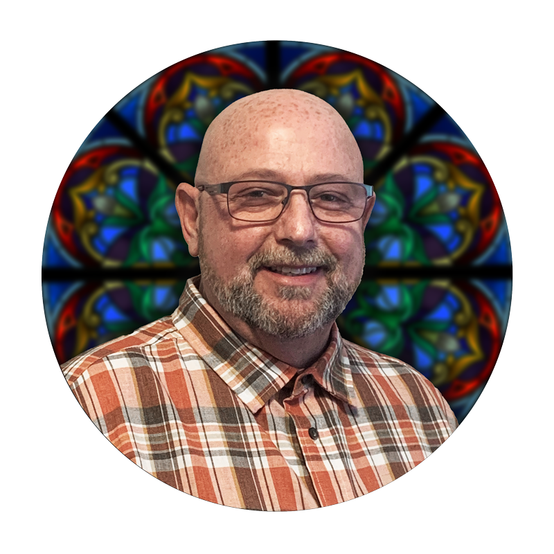 Robert Bohannon, Director of Road Production at Willet Stained Glass Studios, smiling in front of a colorful stained glass background.