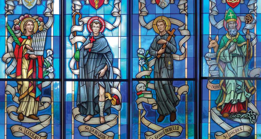 Stained glass window featuring four saints: St. Cecilia with a harp, St. Gerard Majella holding a cross, St. Iderekris, and St. Patrick adorned in green vestments, showcasing vibrant colors and intricate designs, reflecting the artistry of Willet Stained Glass Studios.