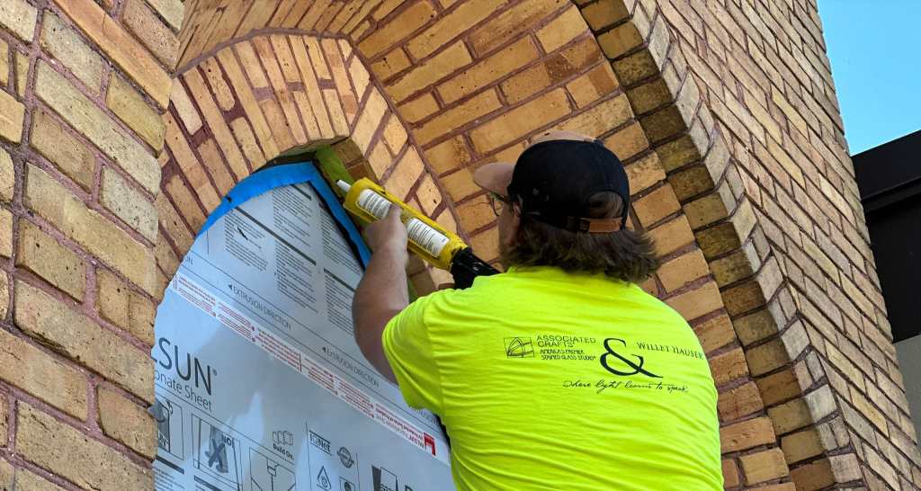 Worker applying protective glazing to a stained glass window during restoration, showcasing preservation techniques and architectural conservation efforts.