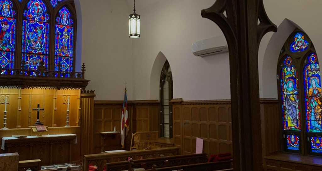 Interior view of a church featuring vibrant stained glass windows depicting religious figures, wooden altar with a cross, and traditional pews, illustrating the artistry and historical significance of stained glass in sacred spaces.
