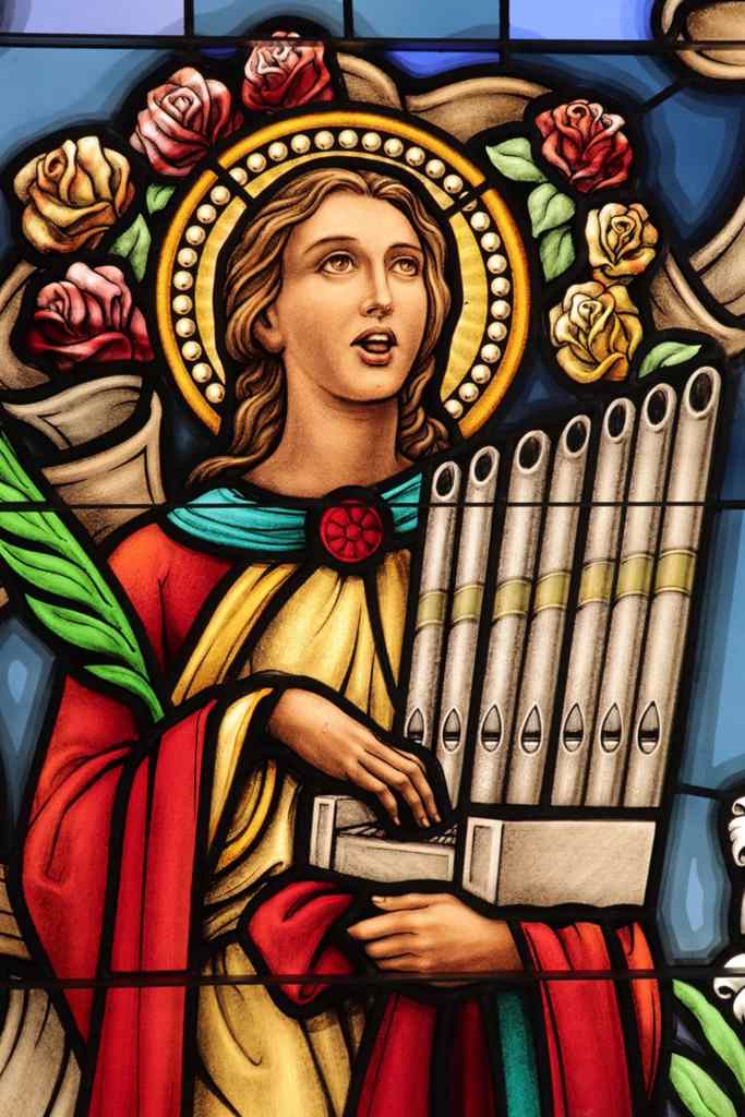 Stained glass window depicting a woman with long hair, holding a pipe organ, surrounded by colorful roses and intricate patterns, showcasing the artistry of Willet Stained Glass Studios.