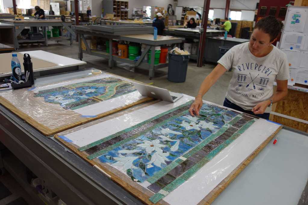 Woman working on stained glass restoration at Willet Stained Glass Studios, surrounded by glass pieces and tools, emphasizing the intricate repair process.