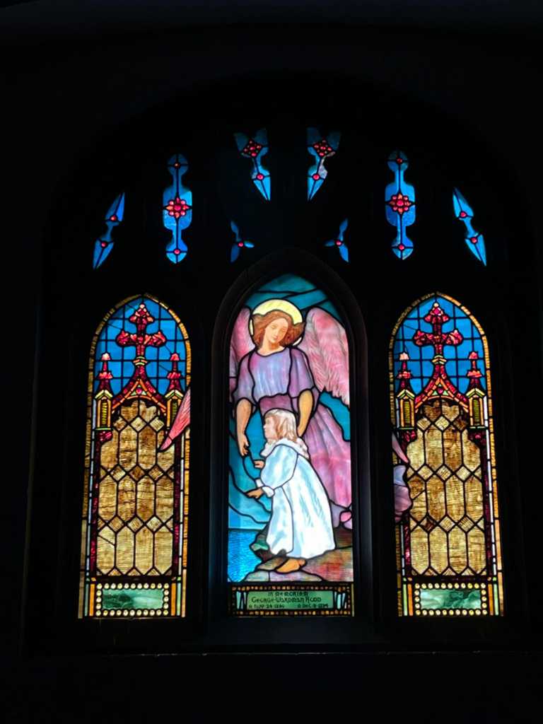 Stained glass window depicting an angel guiding a child, surrounded by intricate geometric patterns and vibrant colors, showcasing the artistry and craftsmanship of Willet Stained Glass Studios.