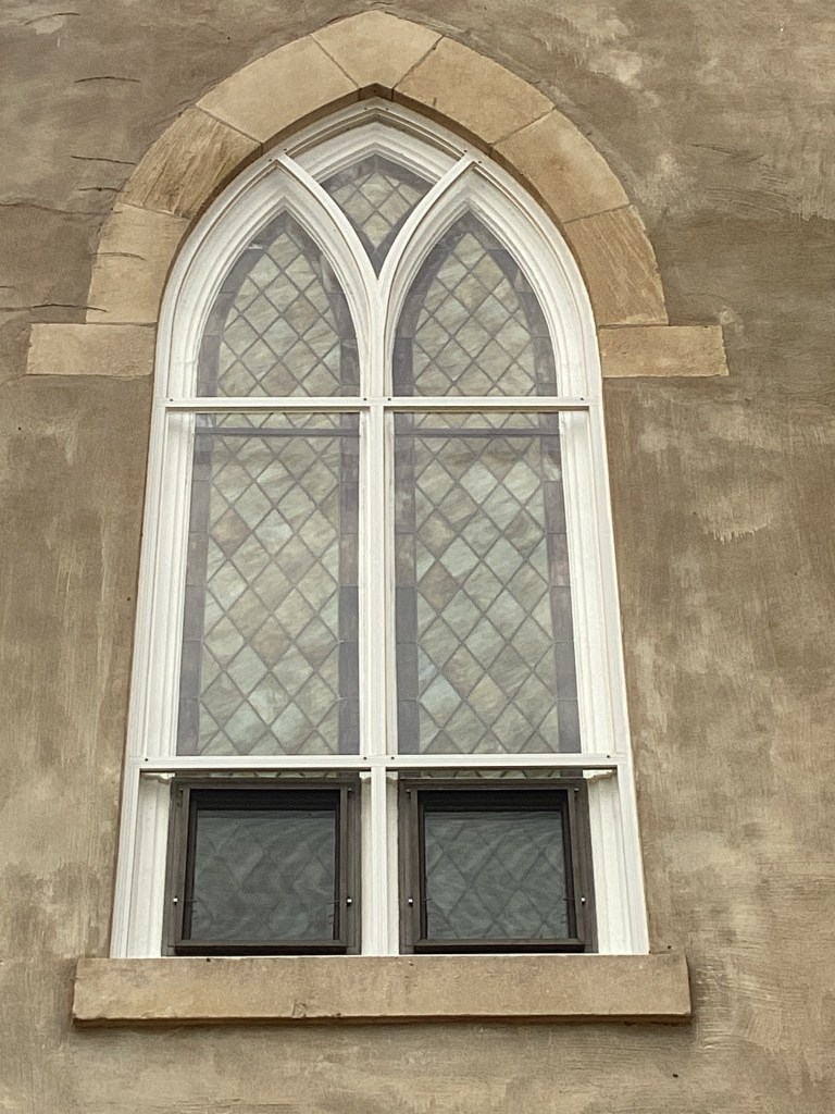 Gothic Revival stained glass window of St. Donatus Catholic Church, showcasing intricate diamond patterns and traditional architectural features.